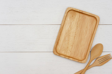 Empty rectangle wooden plate with spoon and fork on white wooden table. Top view image.
