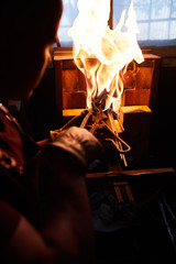 Over shoulder view of busy blacksmith using tongs while putting metal in heated brick furnace