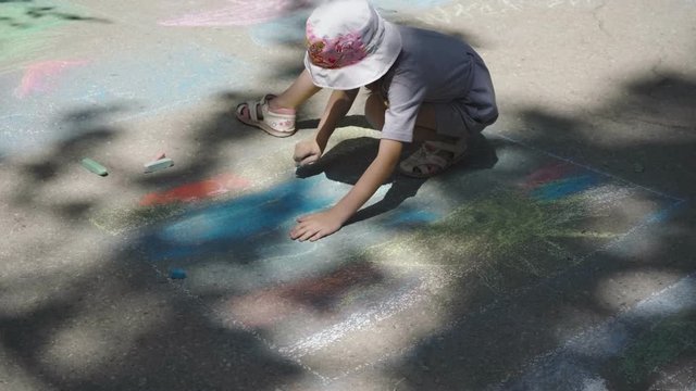Little girl draws on the asphalt drawings in colored chalk