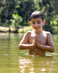 boy stands in the lake and folded his arms in namaste