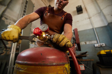 Close-up of busy workman in protective gloves using wrench while changing pressure in gas tank