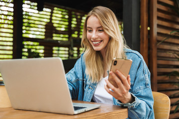 Portrait of nice smiling woman using laptop and cellphone in cafe outdoors