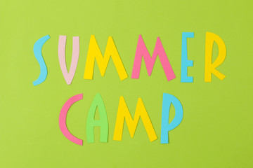 Text SUMMER CAMP of multicolored paper letters on a bright green background. top view. flat lay