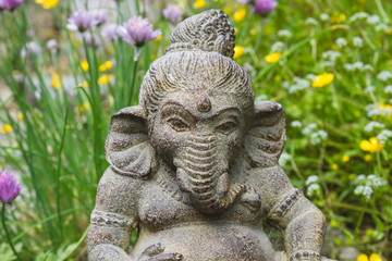 Ganesh stone statue in a garden with flowers