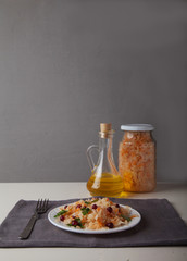fermented cabbage in a glass jar, a fork and a plate with cabbage and cranberries on a white table on a gray background