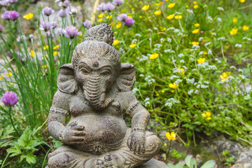Obraz premium Ganesh stone statue in a springtime garden with flowers