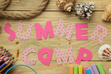 Text SUMMER CAMP of multicolored paper letters and rope and colored chalk on a natural wooden background. top view. flat lay