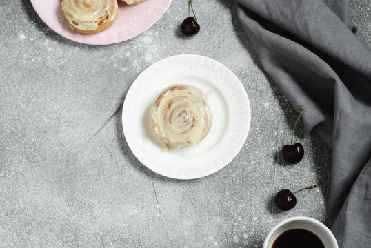 Cinnamon buns on round plates and a cup of coffee on a gray background, decorated with a linen towel and sweet cherry. Horizontal image. Flat lay. Copy space.