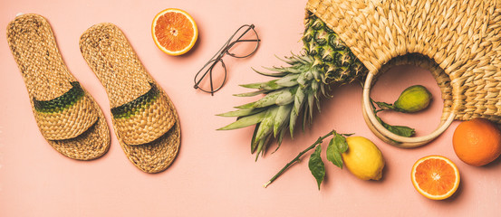 Summer apparel items. Flat-lay of summer flip flops, sunglasses, wicker bag and fresh fruits over pastel pink background, top view. Summer beach vacation concept