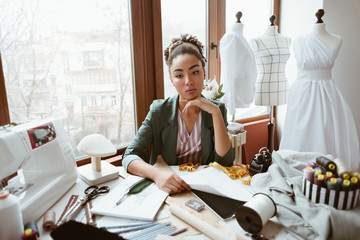 Fabulous young tailor in design studio. Young woman near sewing machine