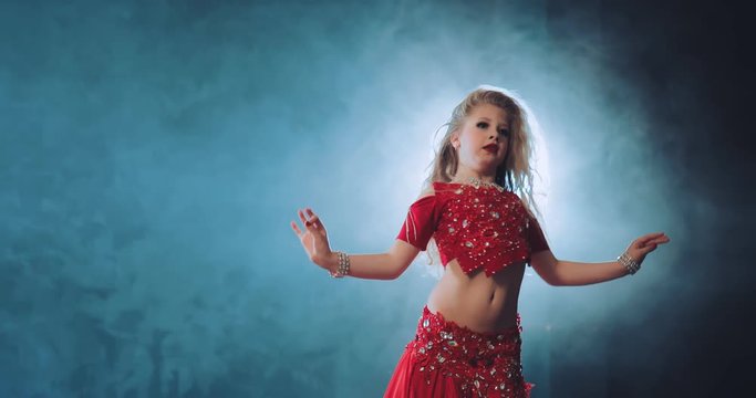 Little beautiful girl dancing oriental dance in a beautiful suit with stones. Young dancer smiles and shakes belly.