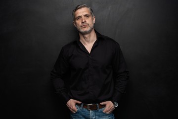 Middle-aged good looking man posing in front of a black background with copy space.