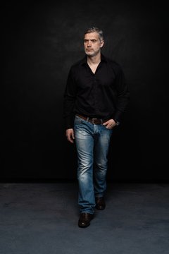 Full Body Portrait Of Middle-aged Good Looking Man Posing In Front Of A Black Background With Copy Space.