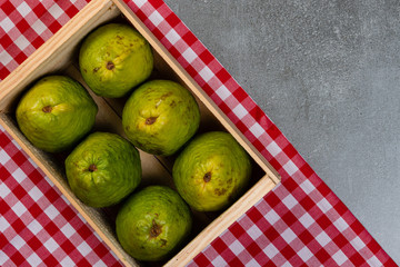 Wooden box with red guavas on concrete background and towel. Concrete texture.