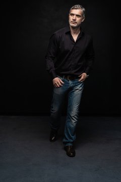 Full Body Portrait Of Middle-aged Good Looking Man Posing In Front Of A Black Background With Copy Space.