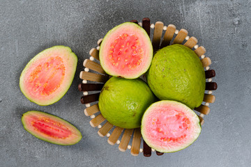 Pot with red guavas on concrete background and towel. Concrete texture. Cut pieces of guava.