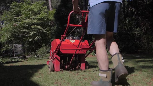 Man using gas powered aerating machine to aerate residential grass yard. Lawn aerationg being performed by groundskeeper using powered landscaping equipment.