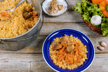 Traditional uzbek meal pilaf rice with meat, carrot and onion in plate on vintage wooden background