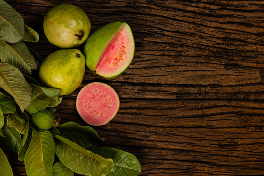 Fresh red guavas with green leaves on wooden demolition background. Wood texture and guava leaves.