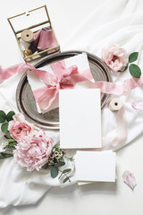 Feminine vertical wedding, birthday mock-up scene. Blank paper greeting cards, eucalyptus, pink roses, peony flowers on white table background.Golden glass box with silk ribbons. Flat lay, top view
