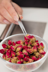 An attractive young female brunette confectioner decorates a white cake with small red flowers of food rose with tweezers.