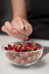 An attractive young female brunette confectioner decorates a white cake with small red flowers of food rose with tweezers.