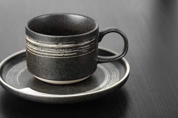 Gray cup and saucer on a black table. Close up with shallow depth of field
