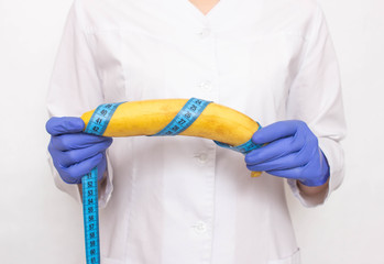 Doctor holds banana in hand with measuring tape. Concept of increasing male penis and operation,...