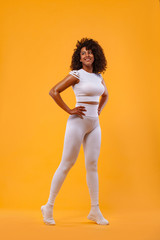Smiling strong athletic woman with black skin and curly hair, doing exercise on yellow background wearing sportswear. Fitness and sport motivation.