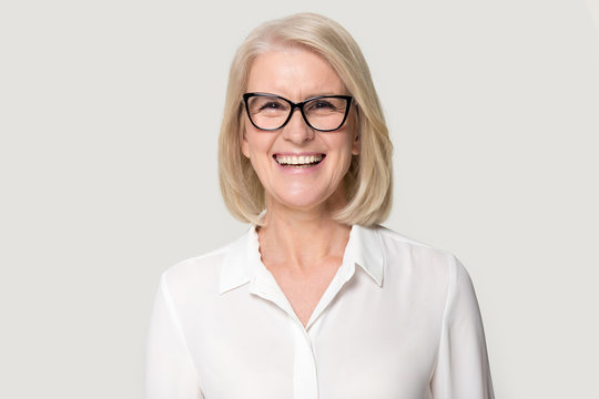 Laughing mature businesswoman wearing glasses posing on grey studio background