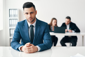 Portrait of confident handsome businessman sitting in office with his business team on background