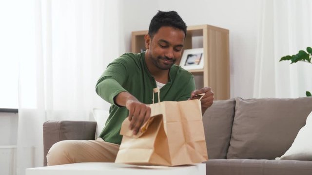 consumption, eating and people concept - smiling indian man unpacking takeaway food at home