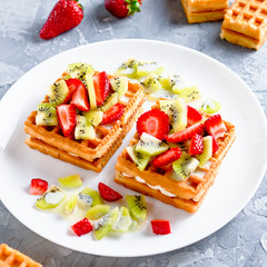 Belgian waffles with fruits strawberries and kiwi on white plate closeup. Tasty healthy breakfast