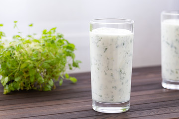 Fresh homemade yogurt (kefir, ayran) in glass with herbs. Ayran, homemade yogurt drink with herbs and cucumbers - healthy summer refreshing cold drink. Probiotic fermented dairy drink. Healthy food. 