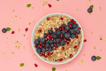 Smoothie bowl with blueberries, pomegranates and granola. Breakfast smoothie bowl on pink background, top view. Vegan diet food concept. 