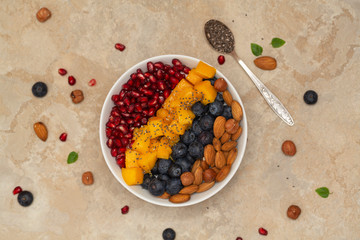 Top view of a smoothie bowl with fresh ripe blueberry, nuts, chia, mango and pomegranate. The concept of healthy eating and lifestyle.  