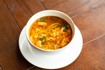 Asian noodle soup with chicken, vegetables and egg in a bowl on a wooden table.