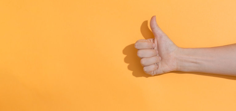 Person Doing Thumbs Up Gesture On A Orange Background