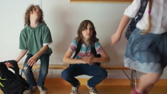 Students during a school break are sitting on a bench in the hallway. Suddenly, the bell rings, children stand and run away to the lesson with their knapsacks