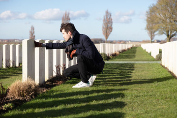 Young man paying respects tombstone on military cemetery