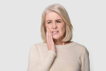 Headshot portrait mature woman touches cheek suffers from tooth ache