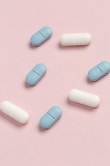 White and blue medical pills on a pink background