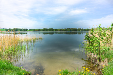 Obraz na płótnie Canvas Beautiful view of the lake, sky, trees, flowers and water grass. Spring, Mazury, Poland.