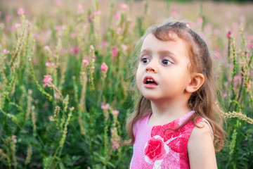 Cute baby girl looks aside outdoors in green field. Child portrait