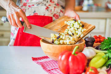 Female hand put cut eggplant in wooden bowl in kitchen. Cooking vegetables