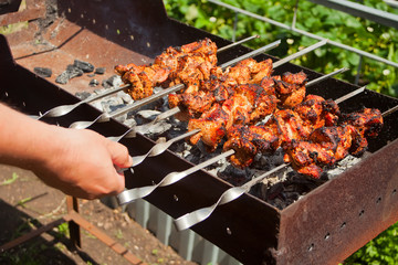 On the barbecue, a lot of meat is roasted on skewers, the chef turns over his shish kebabs. A man's hand turns, fries tasty meat of pork on skewers.