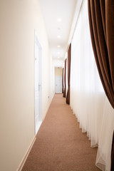 Bright corridor with white doors, brown carpet, white tulle curtains and brown curtains.