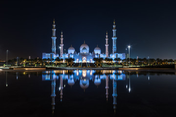 Fototapeta na wymiar Iconic Islamic Site: Grand Mosque in Abu Dhabi, United Arab Emirates at night with a reflection in the pool showing off its beautiful colours of purple in the sky and water.