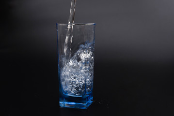 pouring fresh drink water to blue glass on black background