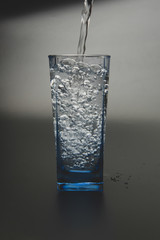 pouring fresh drink water to blue glass on black background
